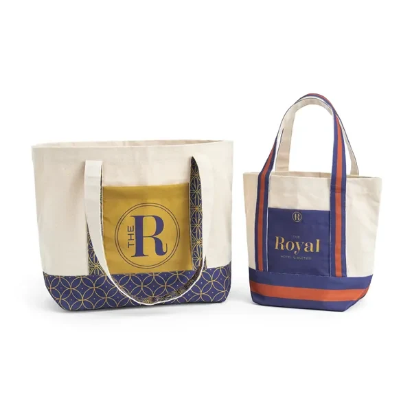Two natural cotton canvas tote bags with navy and gold full color pockets and striped straps, decorated with sample hotel logos