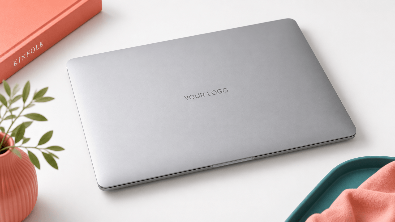 Closed silver MacBook Air on a white desk with a company logo etched in gray at the center of the lid